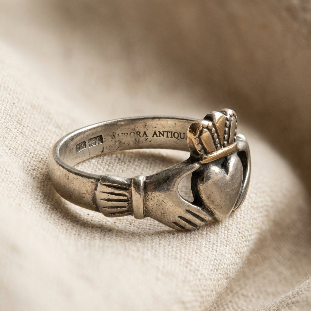 Closeup of an ancient claddagh ring on neutral linen showing aged silver patina and a partial hallmark visible inside the band full frame warm natural lighting