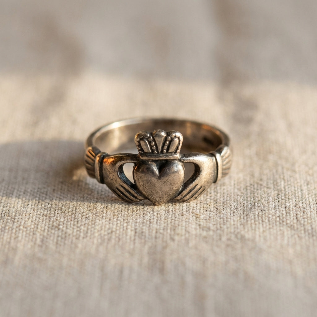 Close up of an ancient order of hibernians ring Claddagh on neutral linen background #ede7da showing heart hands and crown details with warm accent #ae8339