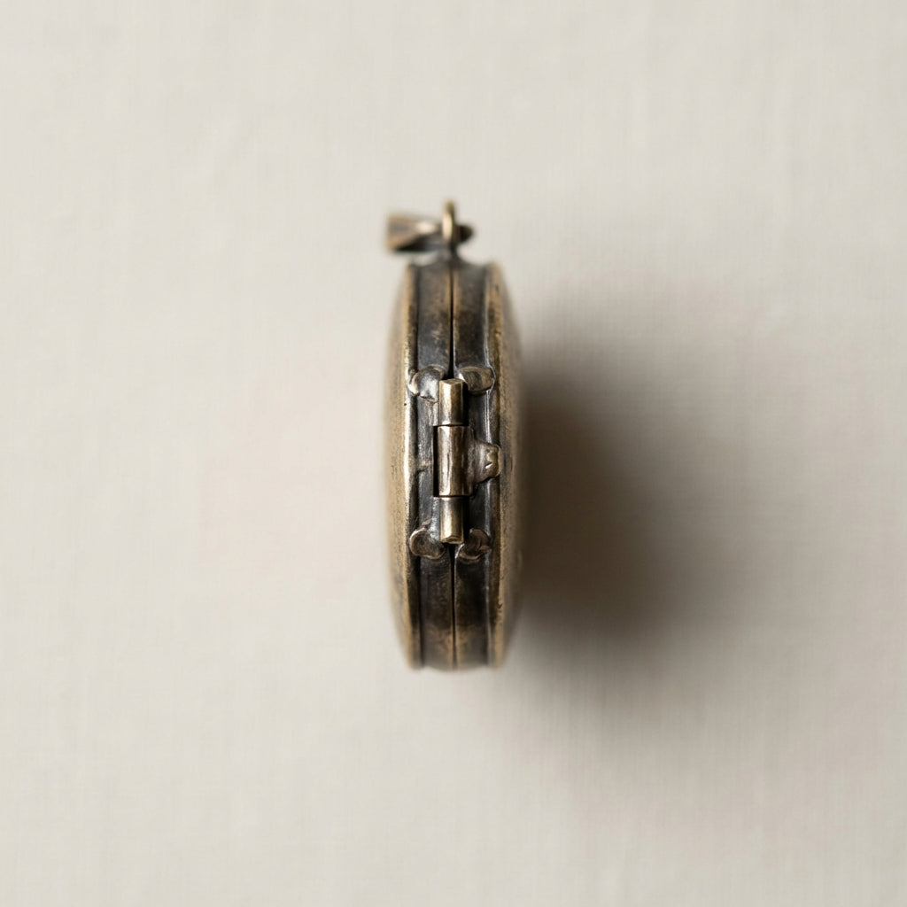 Worn medieval locket pendant close up on minimalist light linen background in beige ede7da showing patina solder joins and hinge detail full frame