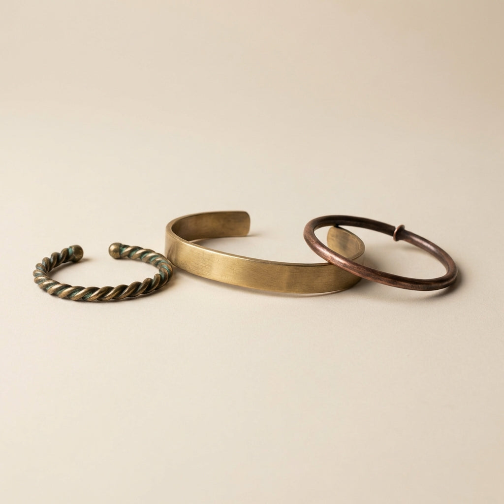 Three old viking jewelry arm rings on a neutral Aurora Antiqua background #ede7da soft side lighting reveals twisted wire torc flat slab bracelet and simple bent hoop emphasizing texture and minimal composition