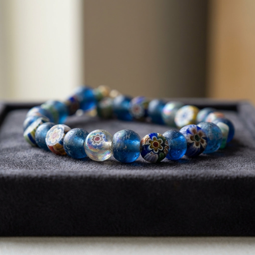 Close up full frame photograph of a roman glass bead necklace of mixed blue and millefiori beads on a dark padded museum tray showing iridescence and fine surface texture