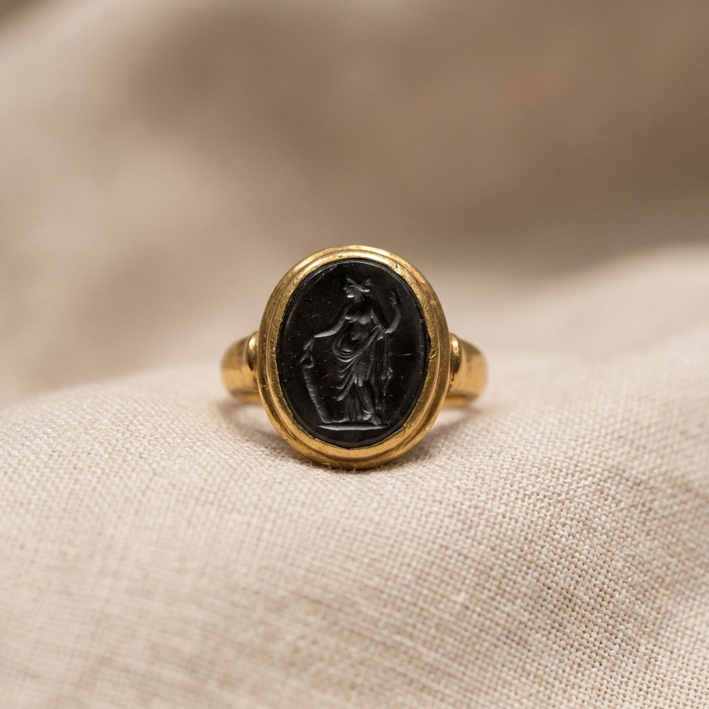 Close up of a roman intaglio ring on fine linen lit by soft museum lighting showing carved gemstone and gold bezel minimalist composition