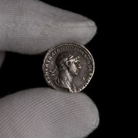 Roman silver denarius of Trajan held for size reference.