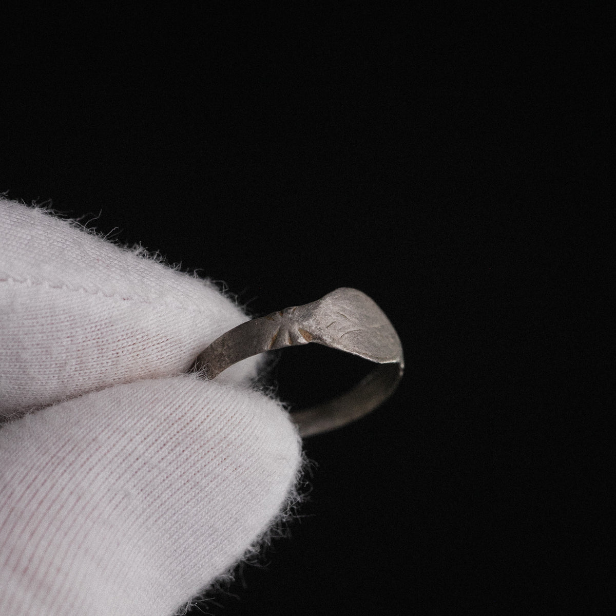 Close-up of Medieval silver ring Aldwin held in gloved hand, showing bezel wear