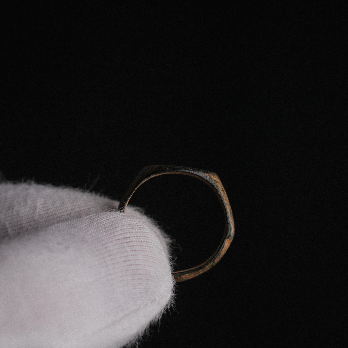 Medieval bronze signet ring Falco held in gloved hand, back view showing hoop taper and patina