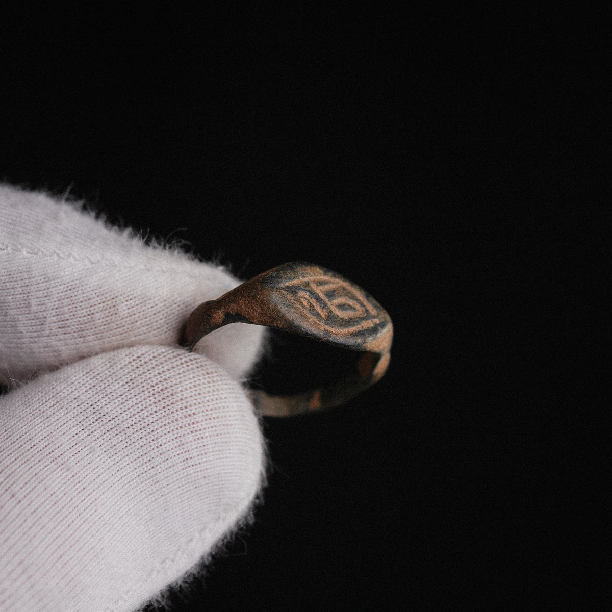 Medieval bronze signet ring Aldren held in gloved hand, close-up of engraved monogram bezel