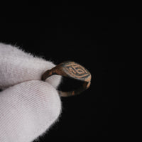 Medieval bronze signet ring Aldren held in gloved hand, close-up of engraved monogram bezel