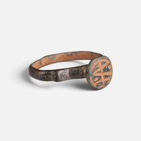 Byzantine bronze ring 'Monogrammos' shows its circular bezel engraving and narrow shoulder at an angle.