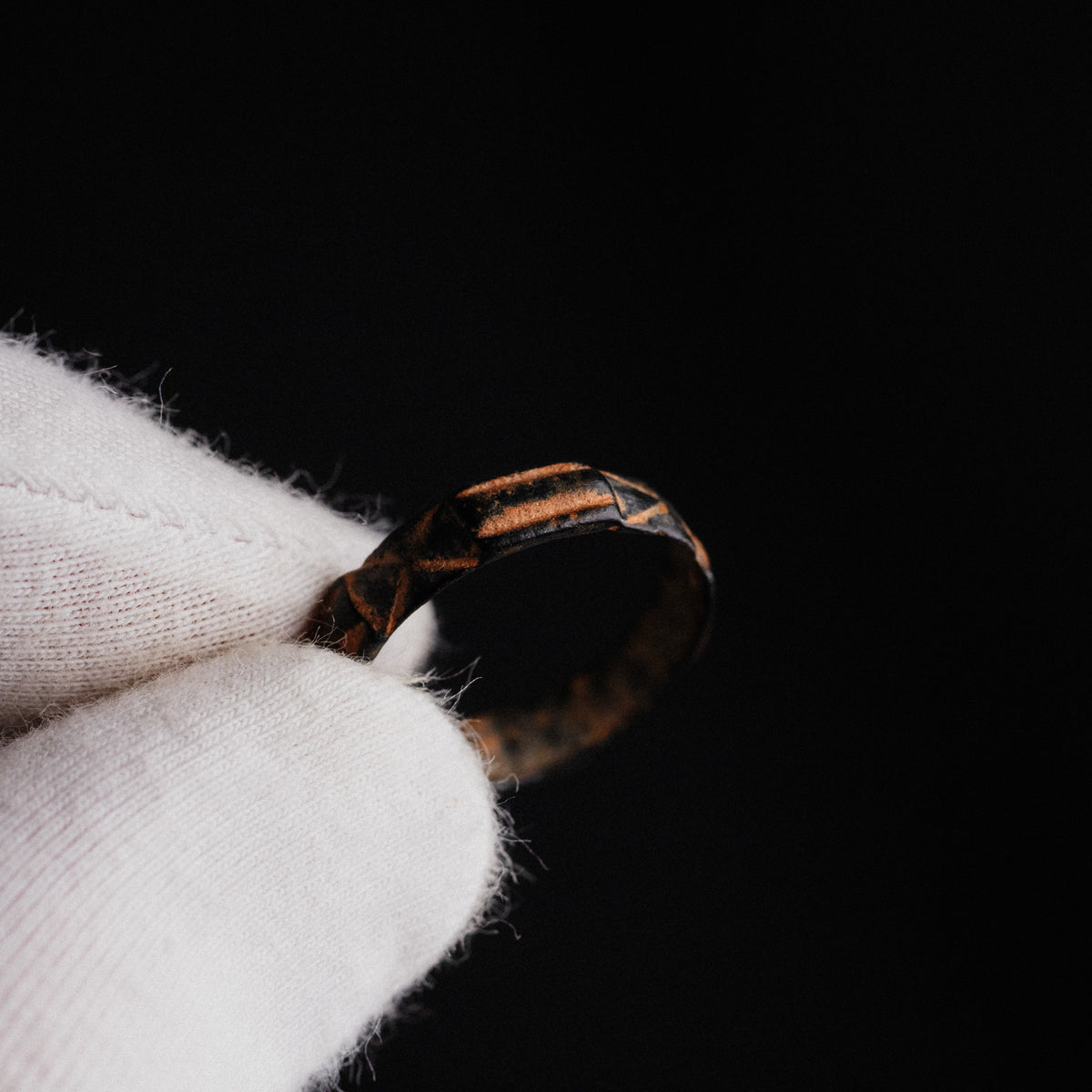 Detail of medieval bronze ring Aldric held in gloved hand, showing warm cuprite highlights