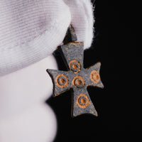 Gloved hand holding medieval bronze cross pendant 'Okellaris' to show ring-and-dot detail