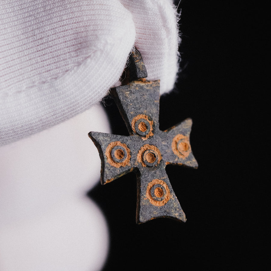 Gloved hand holding medieval bronze cross pendant 'Okellaris' to show ring-and-dot detail
