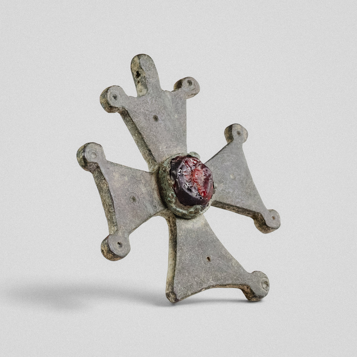 Medieval bronze cross 'Gemmata' angled view showing concave arms and raised central collet with red stone.