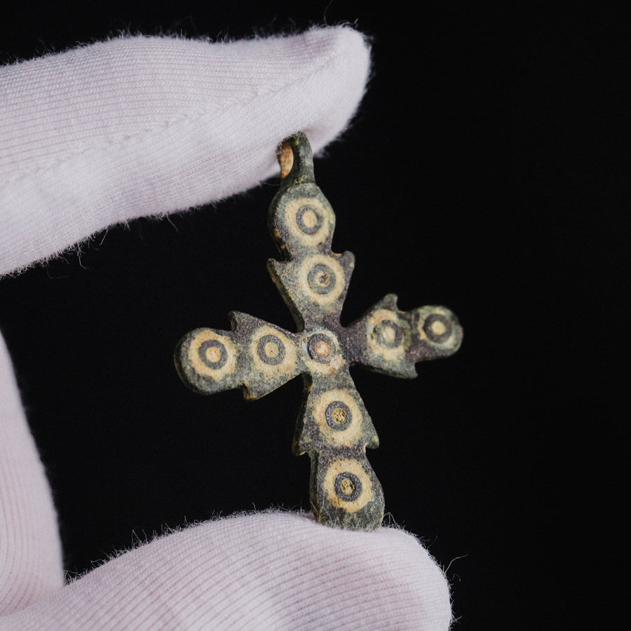 Medieval bronze cross pendant 'Rotunda' held in a gloved hand, showing scale and ring-and-dot detail