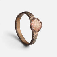 Medieval bronze ring 'Luminara' shows its pale reddish setting and diagonally marked hoop at an angle.