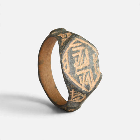 Medieval Islamic bronze ring 'Nasirun' shows its angular bezel engraving and complete broad hoop at an angle.