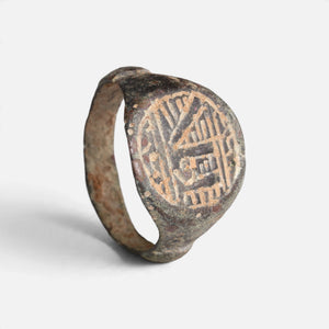 Medieval Islamic bronze ring 'Tahir' shows its dense angular bezel engraving and complete hoop at an angle.