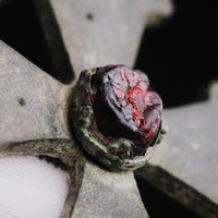Macro of the red cabochon in its beaded collet on medieval bronze cross pendant 'Gemmata', held in a gloved hand