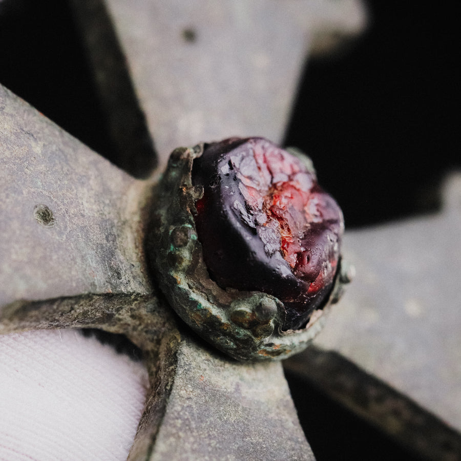 Macro of the red cabochon in its beaded collet on medieval bronze cross pendant 'Gemmata', held in a gloved hand
