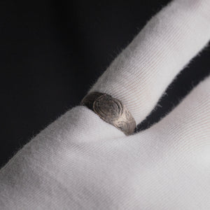 Silver band ring 'Ovata' shows its oval engraving while worn on a white-gloved finger.