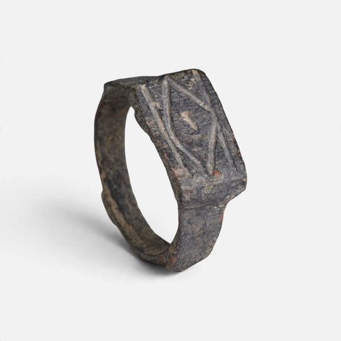 Roman bronze ring 'Lucina' shows its crossed geometric grooves and complete broad hoop at an angle.