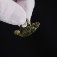 Scale view of Roman bronze pendant 'Felix' held between gloved fingers