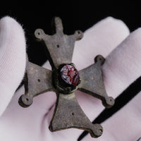 Top-down view of Medieval bronze cross pendant 'Gemmata' with red cabochon and symmetrical flaring arms.