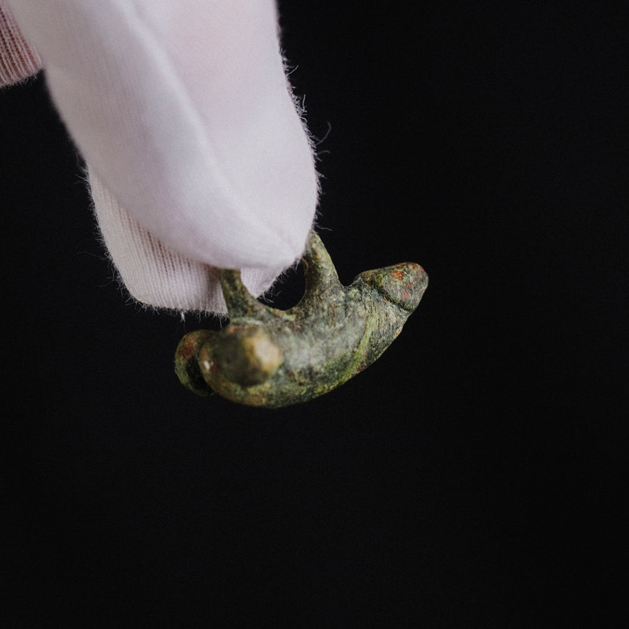 Underside detail of Roman bronze fascinum pendant 'Felix' held in a gloved hand